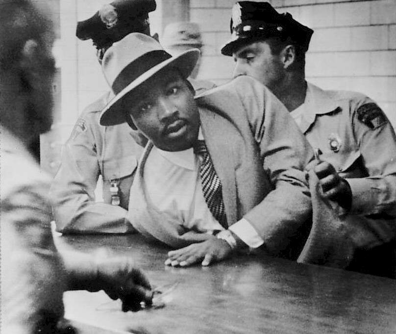 Martin Luther King in handcuffs and pushed against a table by two white police officers.